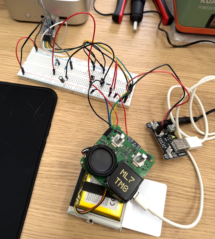 An opened Yoto Mini on a workbench, with its display, speaker, battery and test wiring exposed for flashing open source firmware